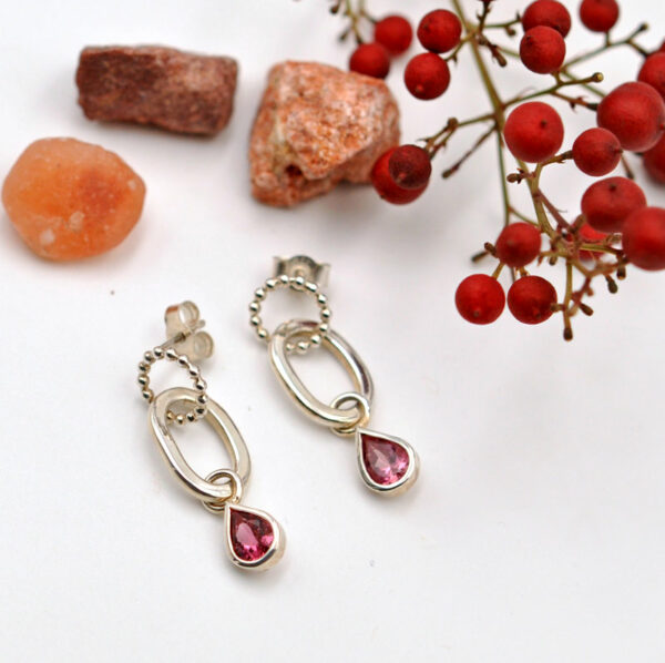 Une paire de boucles d'oreille en argent avec une tourmaline rose taille poire, composée de trois anneaux mobiles emmaillés les uns aux autres.